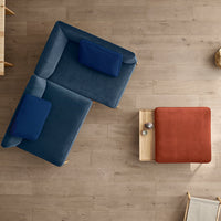 "Blue and navy sectional sofa with a rust-colored accent pillow and wooden coffee table on a light wood floor."