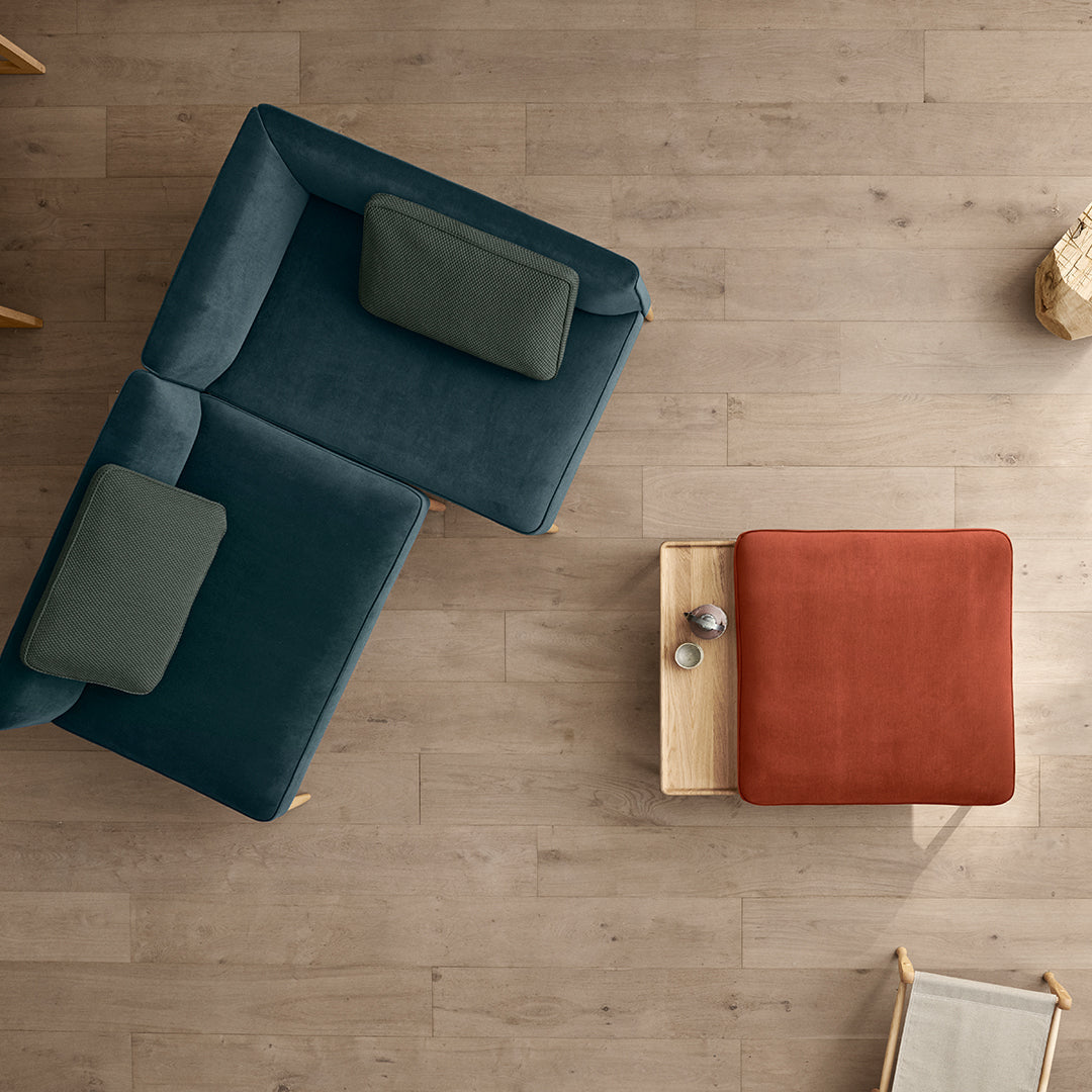 Teal and green sofa with cushions, complemented by a rust-orange ottoman on light wood flooring. Modern, stylish design.