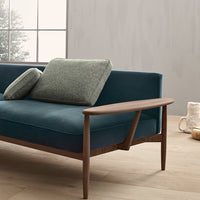 Teal upholstery with two textured green cushions and a wooden armrest, set against a neutral backdrop.