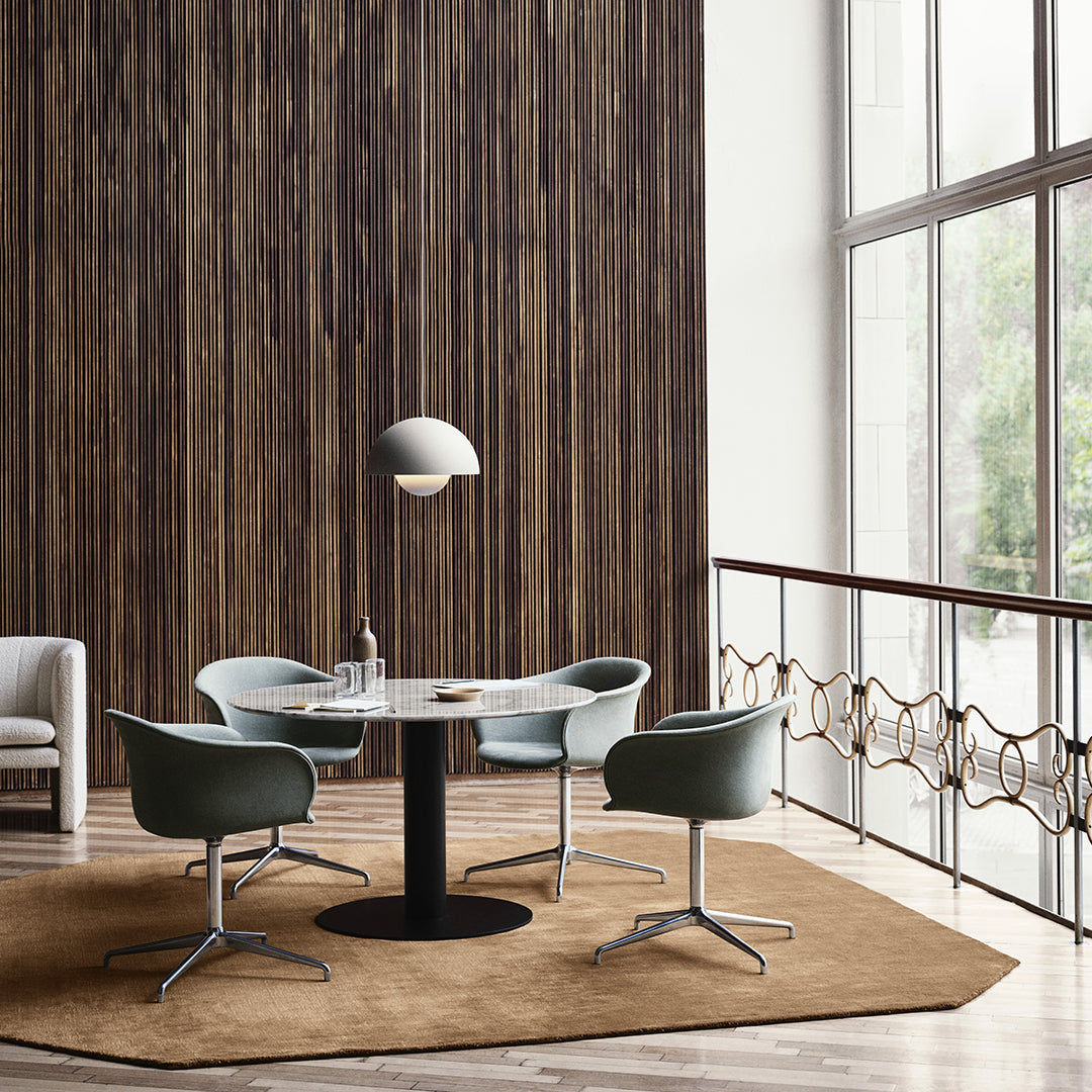 Elegant round table with four blue-green chairs on a soft brown rug, set against a textured wooden wall.