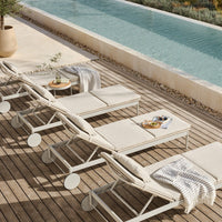 Light beige lounge chairs with soft cushions, set on wooden decking beside a tranquil blue pool and lush greenery.