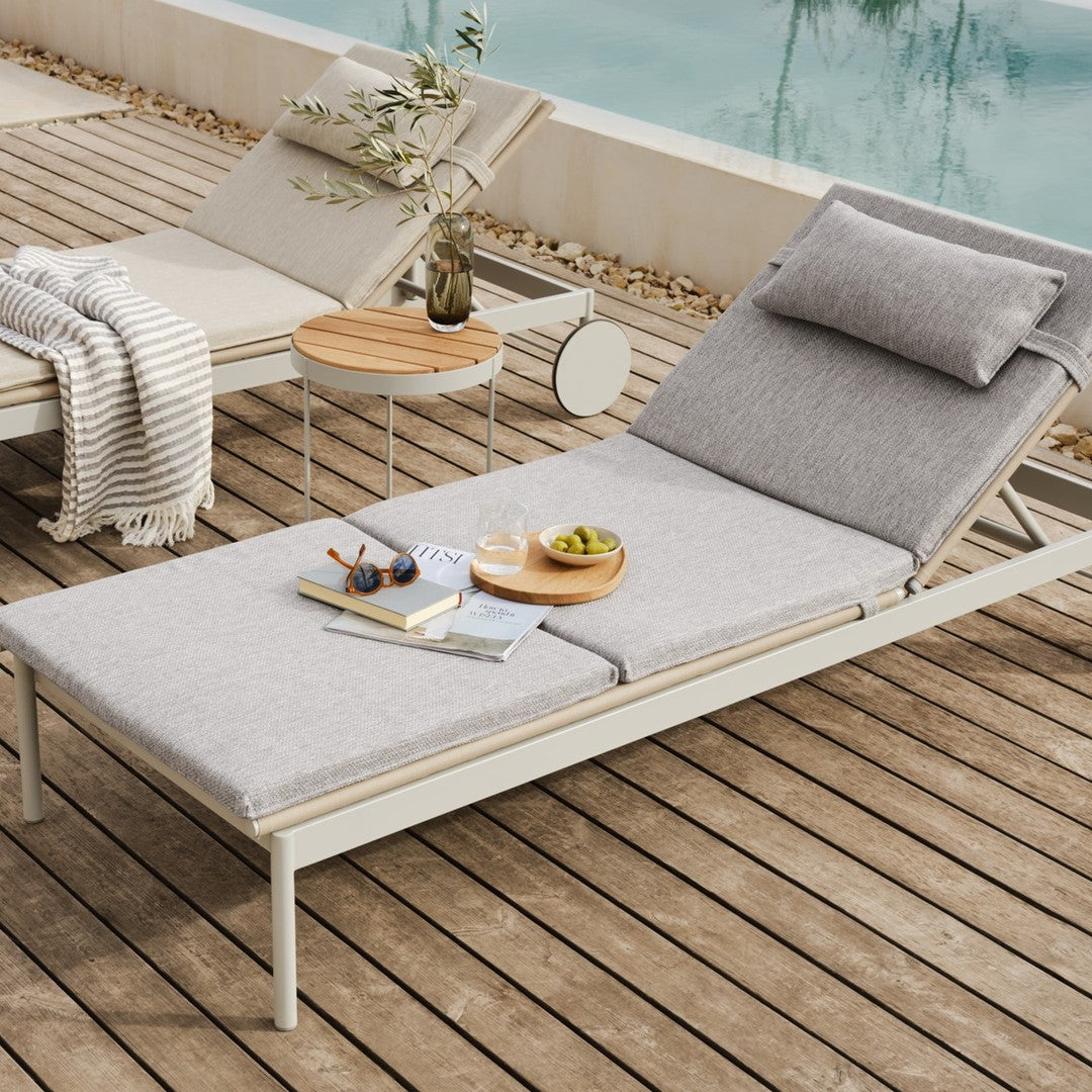 Gray fabric lounge chair with a simple pattern on a wooden deck, surrounded by neutral-toned decor.