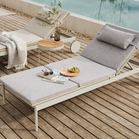 Gray fabric lounge chair with a simple pattern on a wooden deck, surrounded by neutral-toned decor.