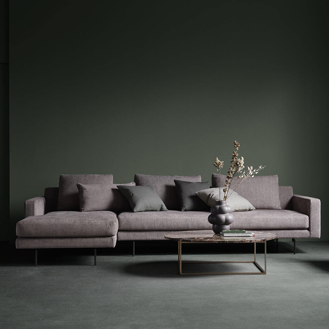 Gray modern sofa with plush cushions, set against a dark green wall and featuring a minimalist glass coffee table.