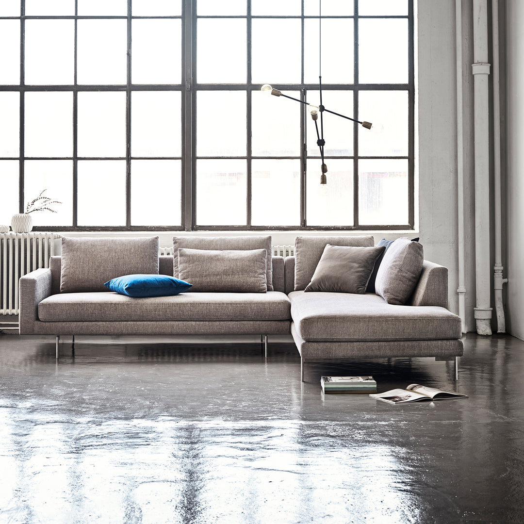 Modern light gray sectional sofa with a textured pattern and a vibrant blue accent pillow, set against a bright industrial backdrop.
