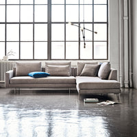 Modern light gray sectional sofa with a textured pattern and a vibrant blue accent pillow, set against a bright industrial backdrop.
