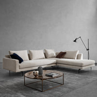 Light beige sectional sofa with textured fabric, accented by dark blue and deep burgundy cushions, set against a gray backdrop.