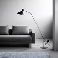 Modern black floor lamp beside a gray sofa, with a light blue textured rug on a neutral floor. Minimalist design and colors.