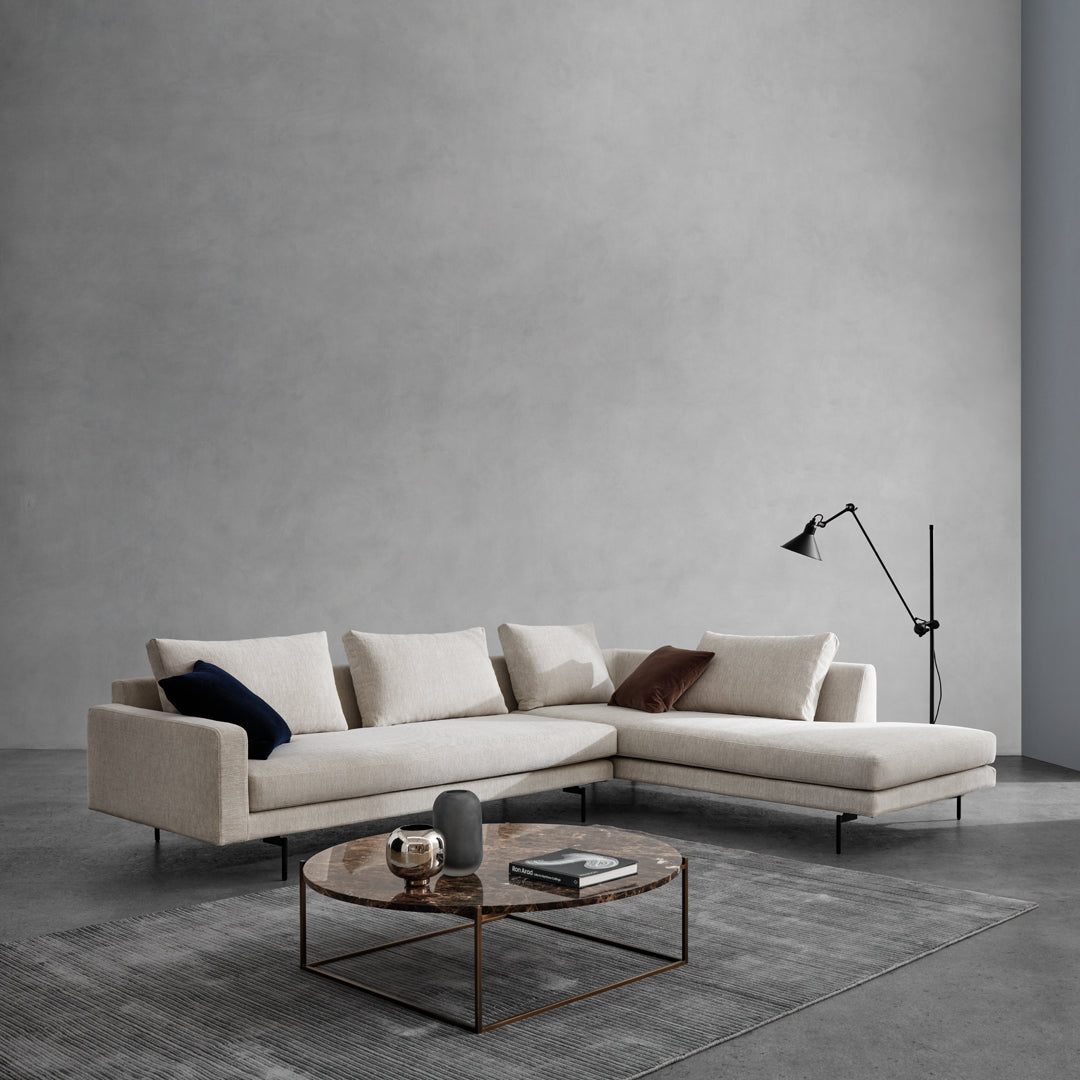 Beige sectional sofa with navy and rust accent pillows, set against a minimalist gray wall and concrete floor.
