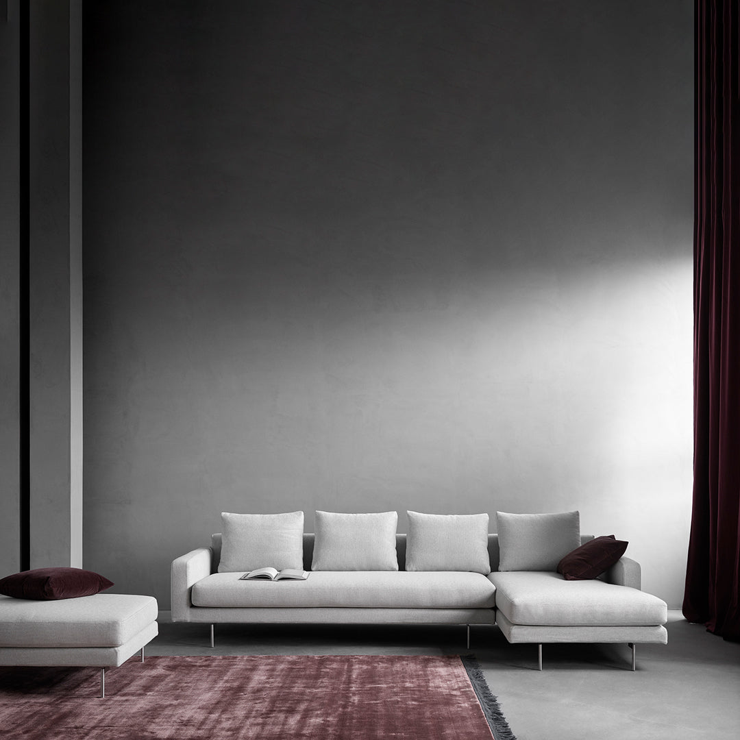 Modern gray sofa with white cushions, paired with a burgundy accent pillow and a textured pink area rug.