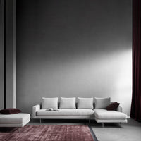 Modern gray sofa with white cushions, paired with a burgundy accent pillow and a textured pink area rug.