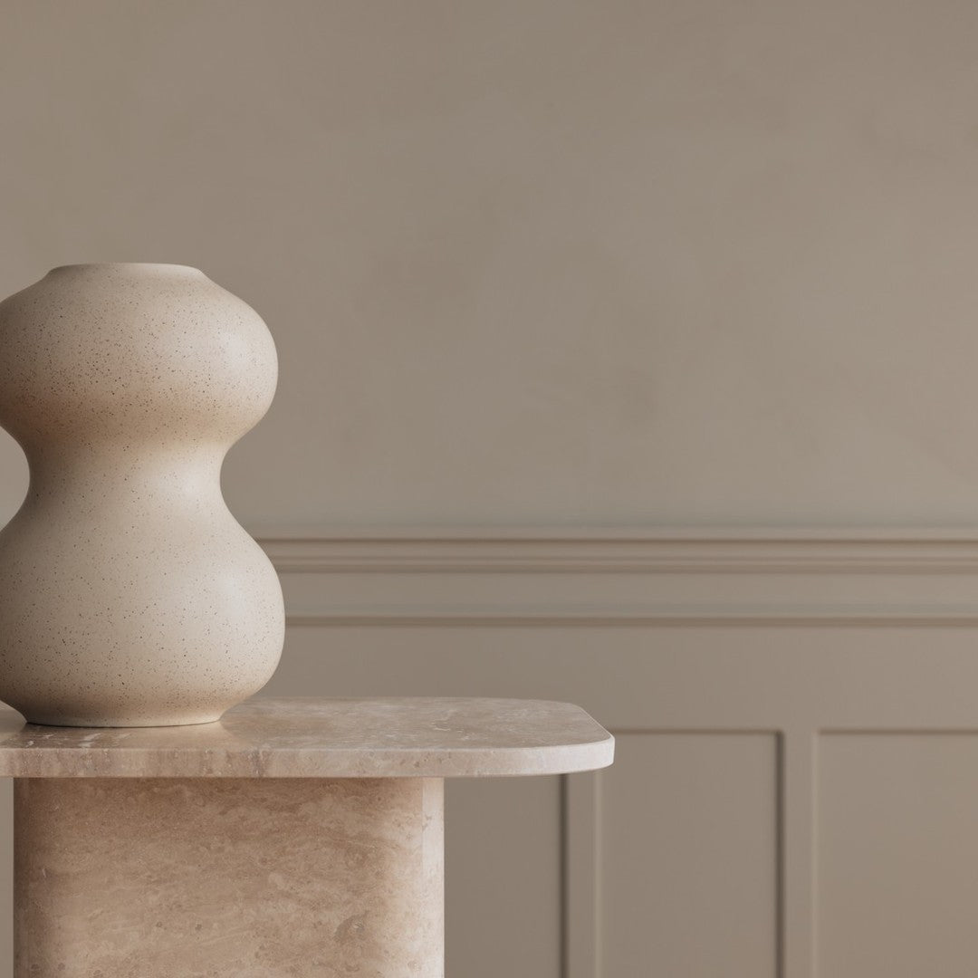 Beige sculptural vase on a light-colored marble pedestal against a neutral, textured wall. Elegant and modern design.