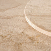 Beige marble surface with subtle veining and a glossy circular edge highlighting natural patterns.