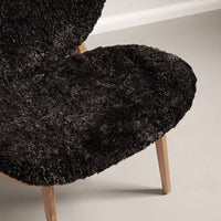 Black textured chair cushion with a plush, shaggy pattern on wooden legs, creating a cozy, modern look.