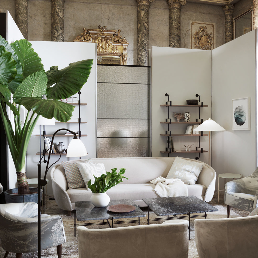 Light beige sofa with textured cushions, green tropical plant, soft gray shelves, and neutral-toned decor in elegant setting.