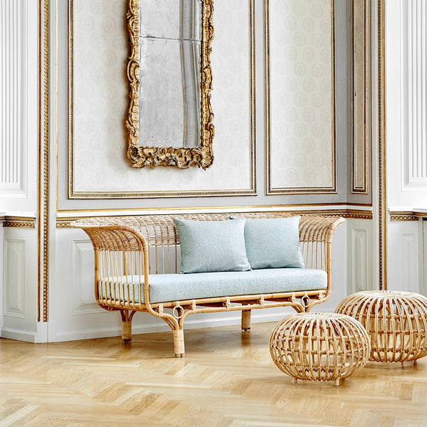 Light blue cushions on a natural rattan sofa, complemented by round rattan poufs against a classic interior backdrop.