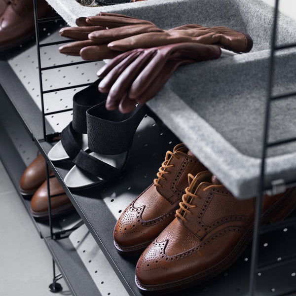 Brown leather dress shoes, black and white sandals, and brown gloves on a modern gray storage shelf.