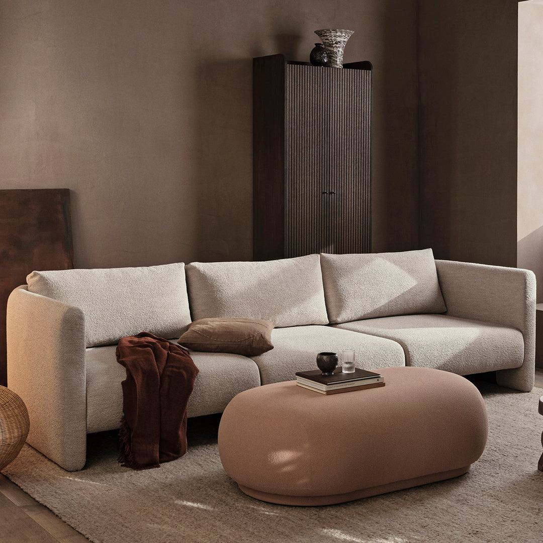 Light beige sectional sofa with smooth lines, complemented by a round, matte peach coffee table and neutral-toned decor.