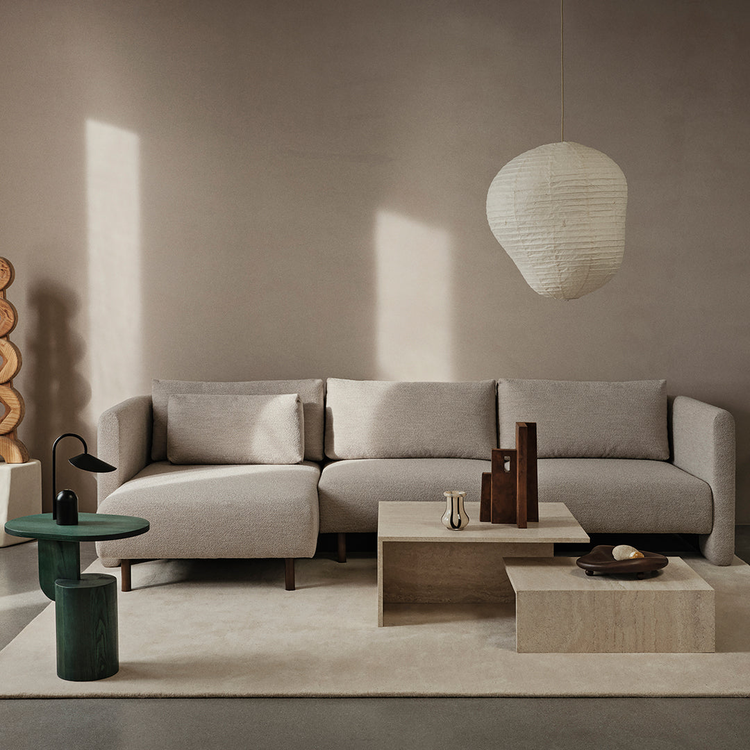 Neutral beige sectional sofa with soft fabric, paired with light wooden tables and a green accent side table.