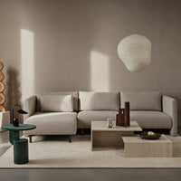 Neutral beige sectional sofa with soft fabric, paired with light wooden tables and a green accent side table.