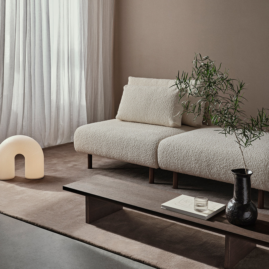 Textured cream sofa with matching pillow against a soft taupe backdrop, complemented by earthy brown and green accents.