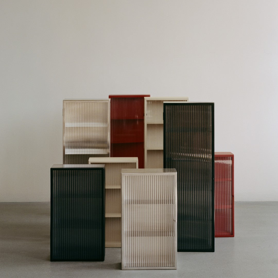 "Stacked cabinets in black, beige, red, and translucent finishes with vertical ribbed patterns."