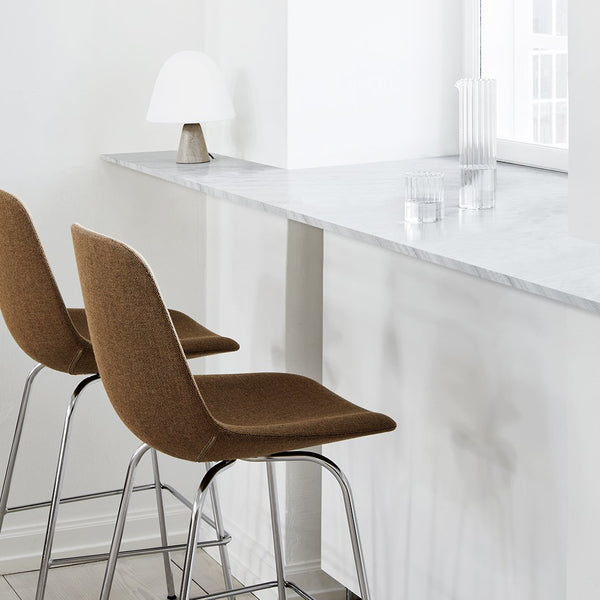 Brown upholstered bar stools with sleek chrome legs against a minimalist white marble countertop.
