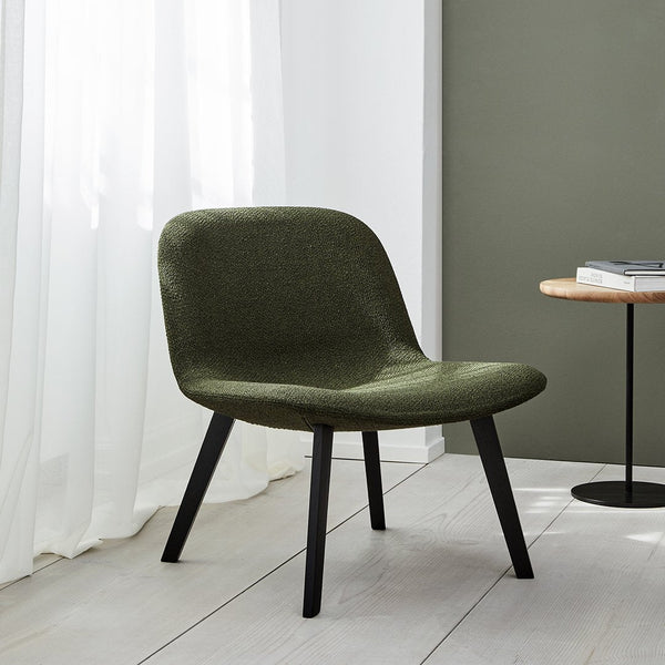 Green upholstered chair with a smooth texture and black wooden legs, set against a light and neutral backdrop.