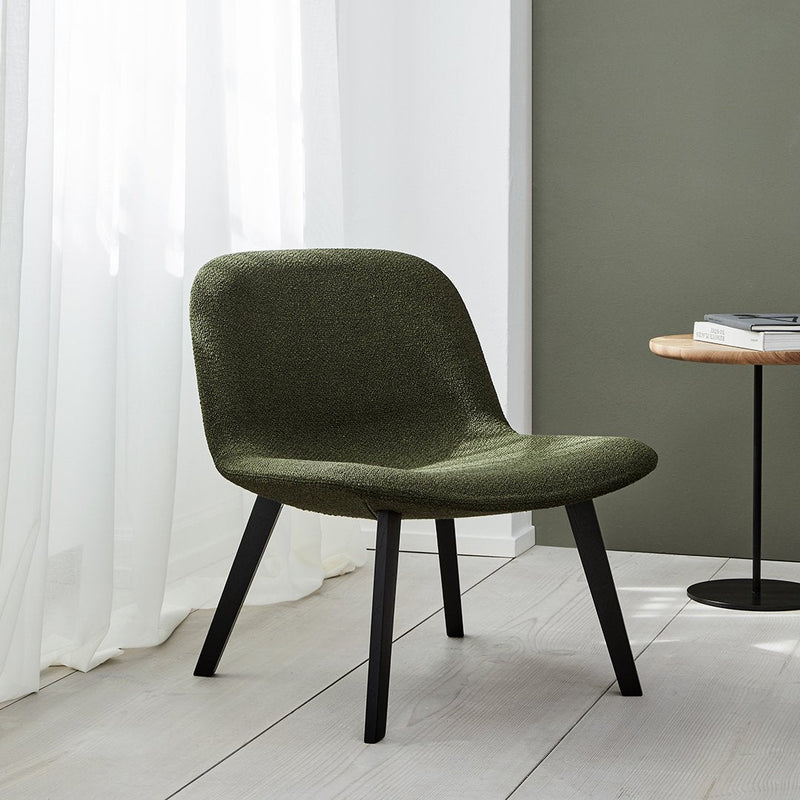 Green upholstered chair with a smooth texture and black wooden legs, set against a light and neutral backdrop.