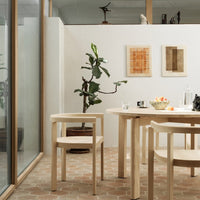 Light wood furniture in neutral tones, complemented by earthy terracotta floor and leafy green plant accents.