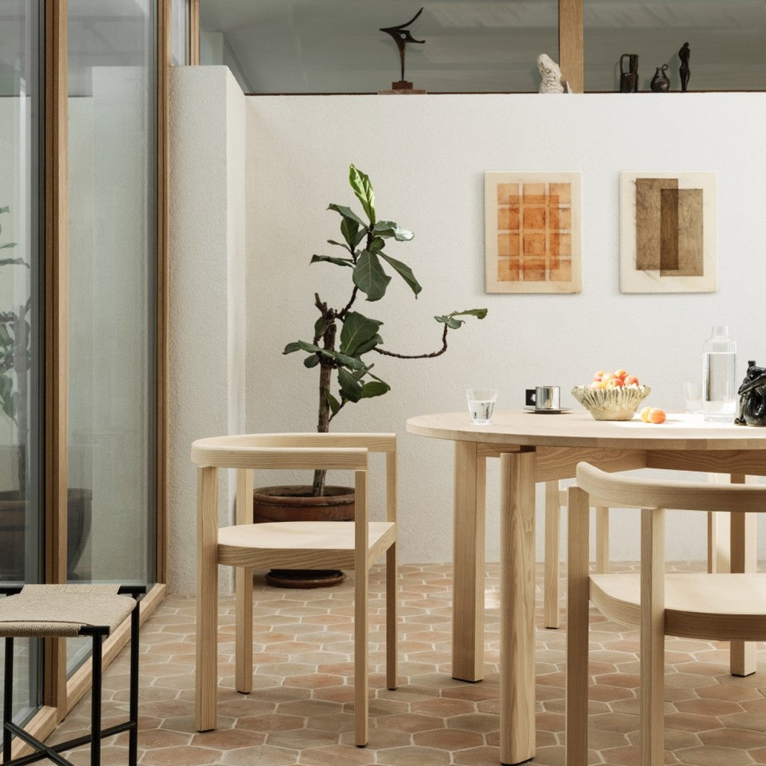 Natural wood tones, earthy terracotta floor, green plant accents, and warm beige wall colors create a serene dining space.