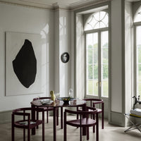 Modern dining area featuring deep burgundy chairs, circular marble table, and a large black abstract artwork.