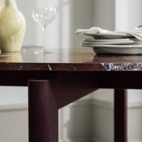 Rich burgundy table legs support a marbled brown tabletop with white veining, complemented by soft gray serving pieces.