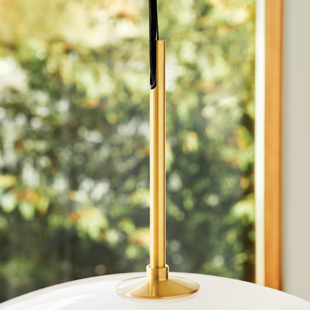 Gold lamp stand with sleek black pendant against blurred green background, highlighting modern design and elegance.