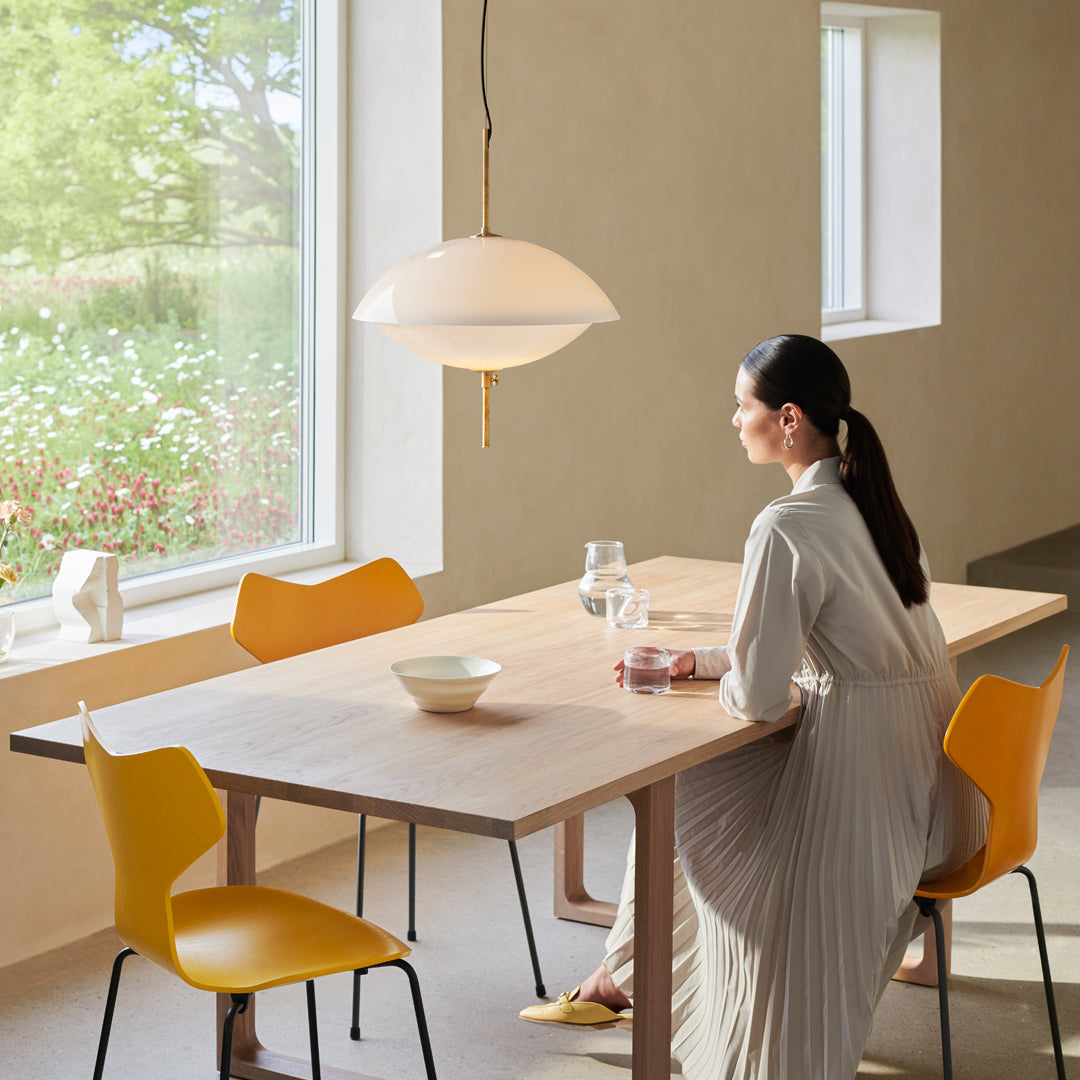 Contemporary wooden dining table with yellow chairs and a modern pendant light in a softly lit, serene setting.
