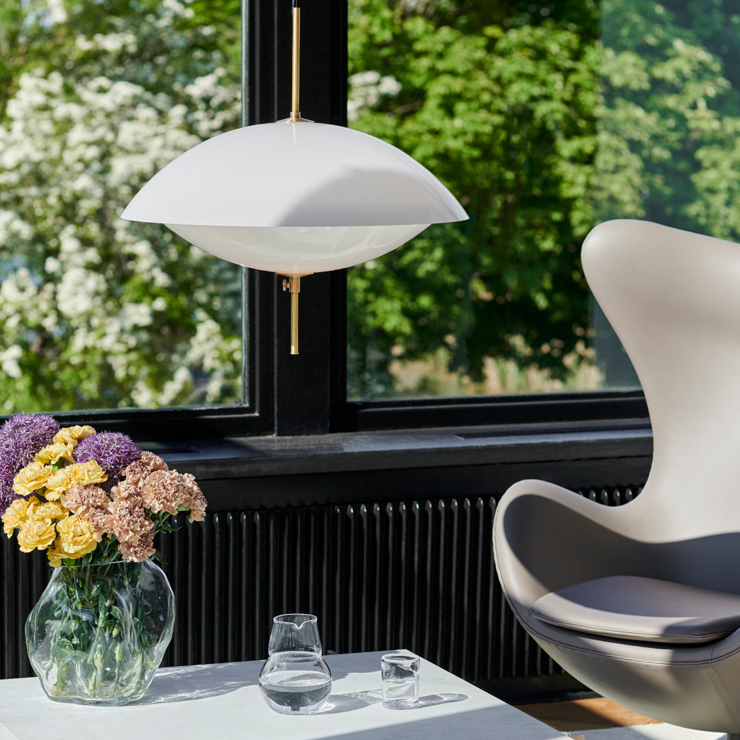 Elegant white pendant lamp with a smooth, curved design, contrasted by a modern gray chair and colorful floral arrangement.