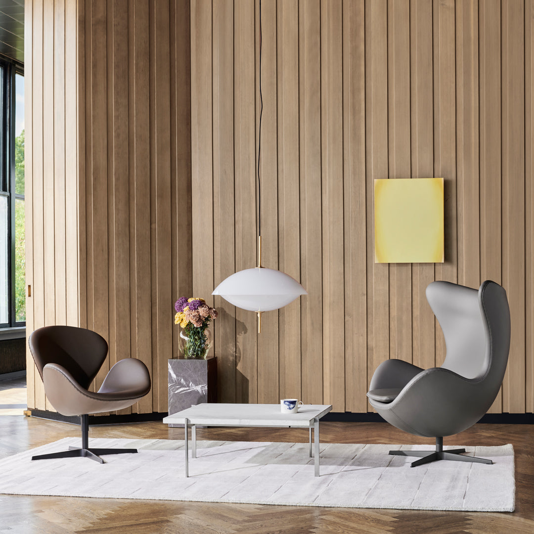 Elegant grey and brown armchairs with a modern white pendant light, set against a warm wooden wall.