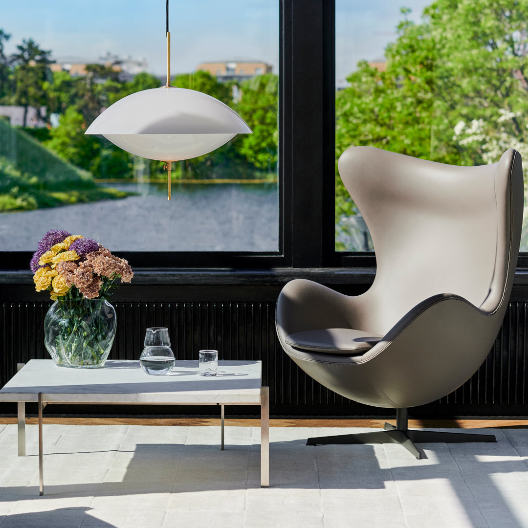 Modern gray and black chair with sleek curves, paired with a clear glass table and a white pendant light. Bright floral accents.