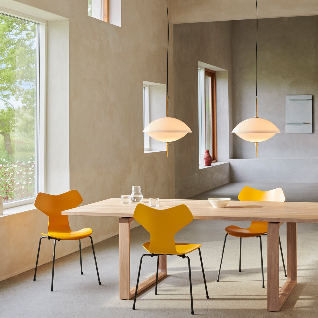Modern dining table setup featuring yellow chairs, warm wood tones, and soft white pendant lights against a neutral backdrop.