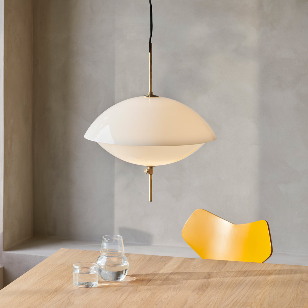 White pendant lamp with a sleek, round shape, featuring a brass accent and set against a soft gray backdrop and yellow chair.