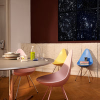 Pastel pink, yellow, and blue chairs around a sleek round table, set against a rich red wall and light wood floor.