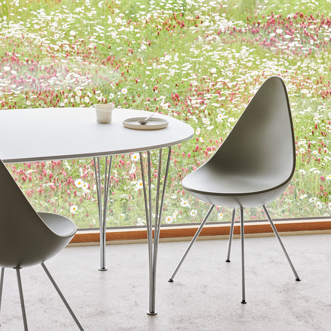 Minimalist gray chair and round white table on a light concrete floor, surrounded by vibrant floral patterns outside.