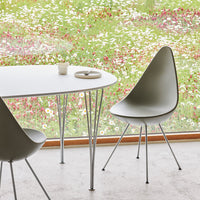 Minimalist gray chair and round white table on a light concrete floor, surrounded by vibrant floral patterns outside.