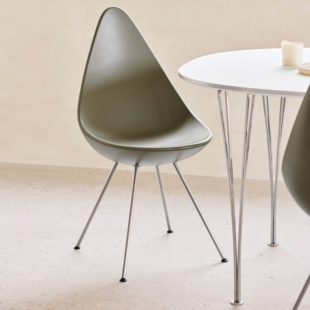 Olive green teardrop chair with sleek chrome legs, set against a neutral background and minimalist white table.