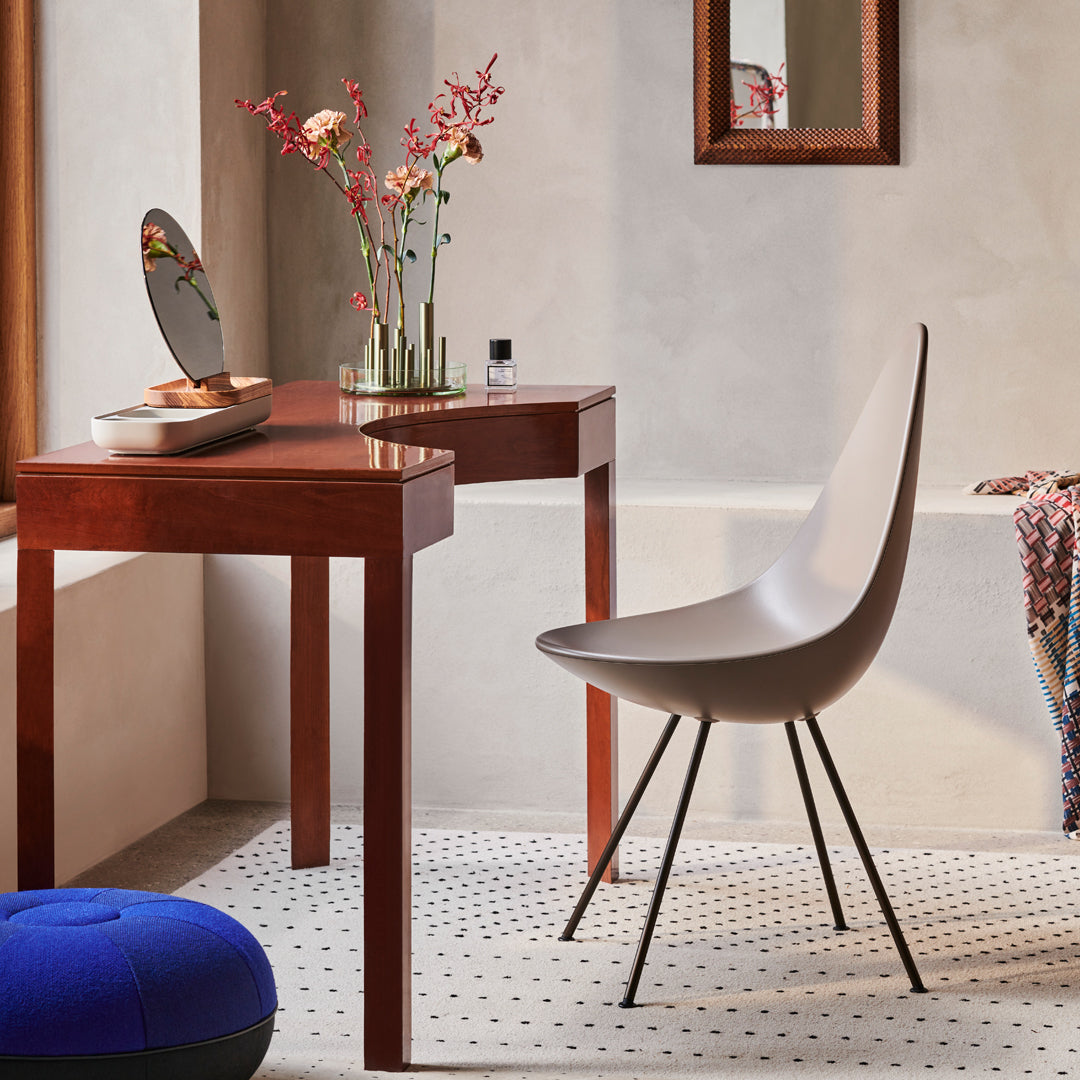 "Elegant white chair with black legs beside a wooden desk, set on a dotted rug with a blue pouf and floral accents."
