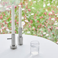 White candlesticks on a sleek silver base, set against a blurred backdrop of vibrant green and pink floral patterns.