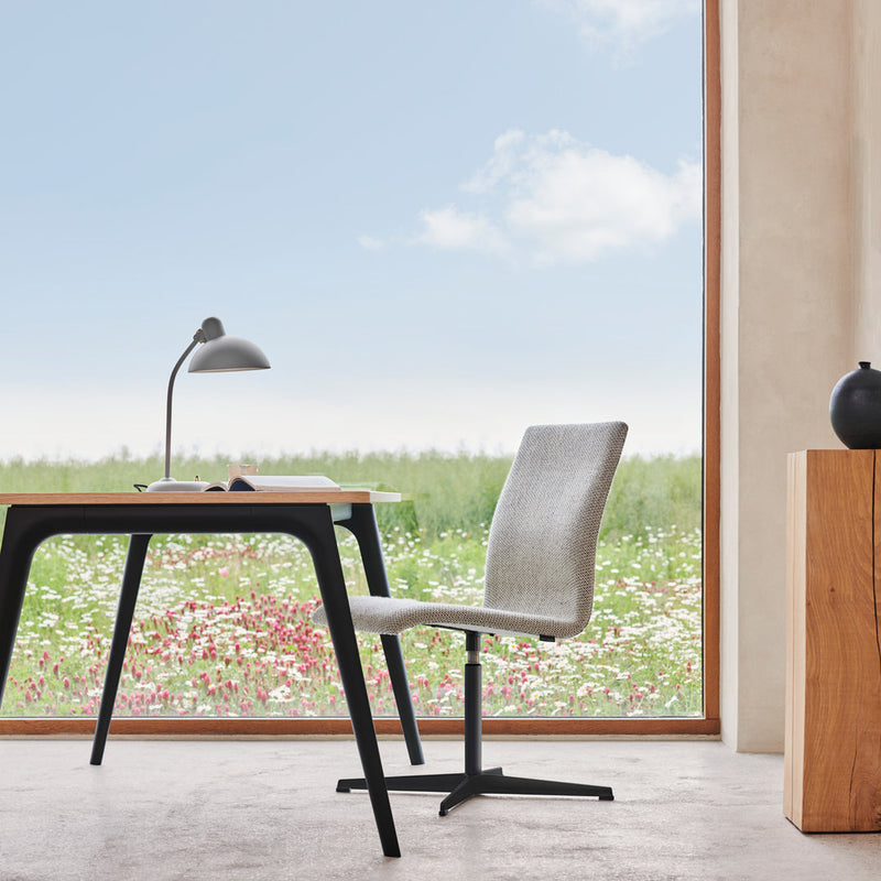 Light gray chair with sleek black accents and a natural wooden desk against a bright, floral outdoor backdrop.