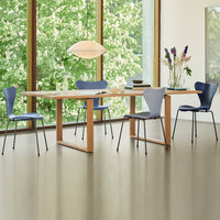 Modern dining room featuring a light wood table, blue chairs, and green outdoor views through large windows.
