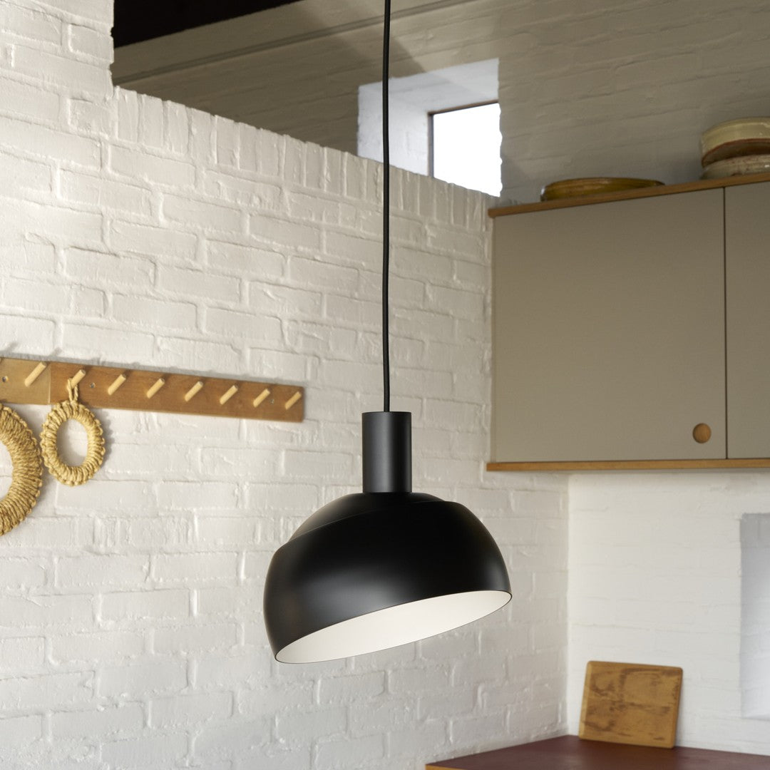 Black pendant light hanging in a kitchen with white brick wall and wooden cabinets.