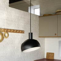 Black pendant light hanging in a kitchen with white brick wall and wooden cabinets.